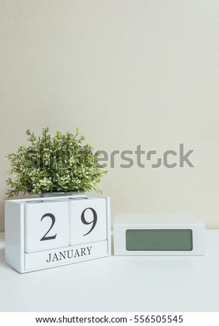 White wooden calendar with black 29 january word with clock and plant on white wood desk and cream wallpaper textured background , selective focus at the calendar