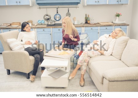 Toned picture of friends girls resting after eating delicious pizza while having party at home. Beautiful ladies ready to sleep after rest or relax. Home party concept.
