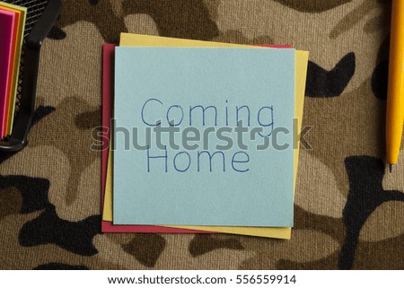  Top view of  Coming Home written note on a camouflage fabric texture.