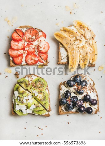 Healthy breakfast toasts. Wholegrain bread slices with cream cheese, various fruit, seeds and nuts. Top view, grey marble background. Clean eating, vegetarian, dieting concept
