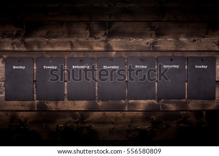 Seven day black chalkboard notices individually hanging from a rustic wooden wall