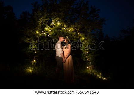 Couple in love staying near tree with lights and holding hands. Riddle of love.