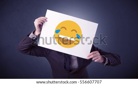 Young businessman hiding behind a laughing emoticon on cardboard