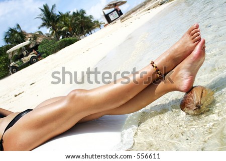 Woman's legs resting on a coconut in tropical water
