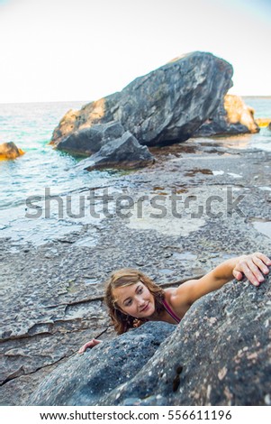 A beautiful woman goes bouldering while rock climbing on the shore line of the Great Lakes. 