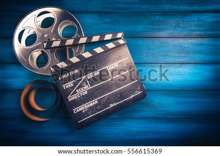 35mm film, reel and movie clapper with dramatic lighting on a wooden background