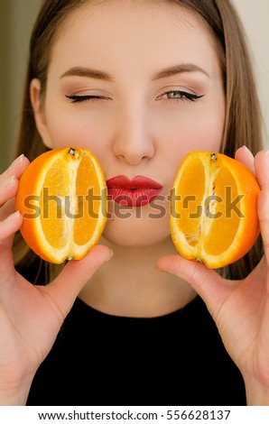 Young beautiful girl closeup portrait with orange fruit, red lipstick and perfect makeup, positive photo with long hair model, sends a kiss