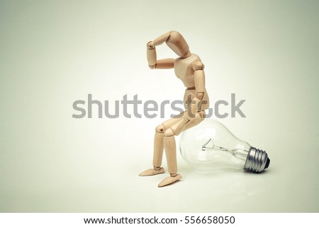 Wood Figure Mannequin sitting on an incandescent light bulb / Being stupid / Having no idea Royalty-Free Stock Photo #556658050