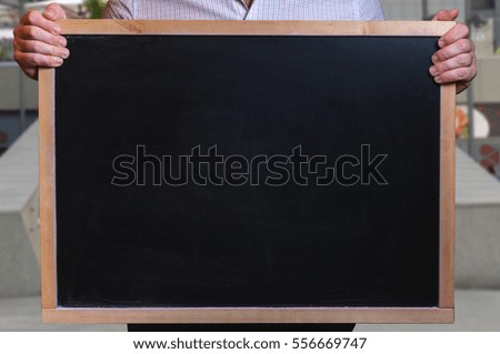 The man (businessman, student or office worker) holding a black chalkboard with free space for your text (blank)