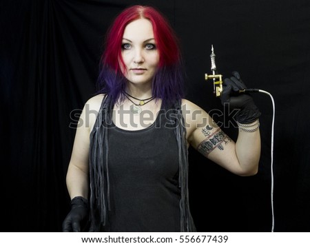 Tattooed girl with red and violet hair in different poses with tattoo machine as tattoo master. Master works. Black background and sterile black gloves. Emotional face. Tattoo glasses.