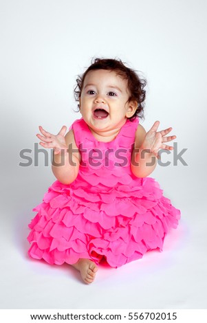 A happy and beautiful baby sits on a white background and blows kisses with hands out.  She looks like she could be clapping.