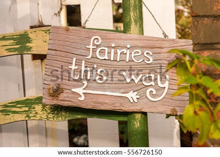 Hanging wooden sign hanging on a old chair in garden that says fairies this way. 