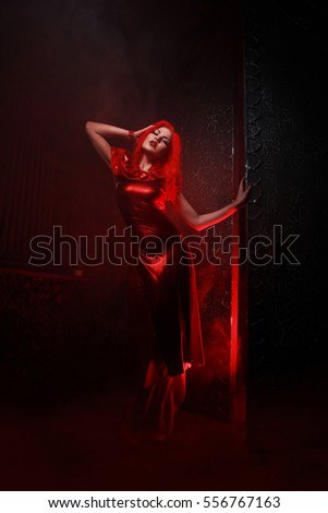 Pretty Red Hair Woman Wearing Red Evening Long Dress Standing In The Night Street Near The Open Gates