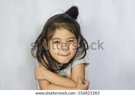 a close up head shot of funny little girl holding herself isolated on grey background
