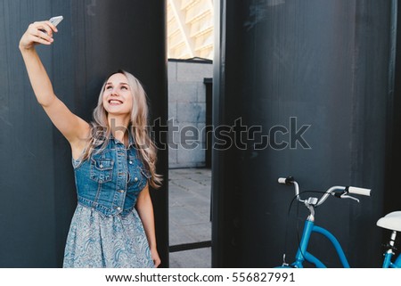 Lifestyle and technology. Young pretty blonde woman taking selfie on smartphone standing with her vintage bike. Good day for a ride. Copy space.
