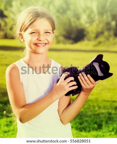 portrait of smiling girl in elementary school age holding photo camera in hands outdoors