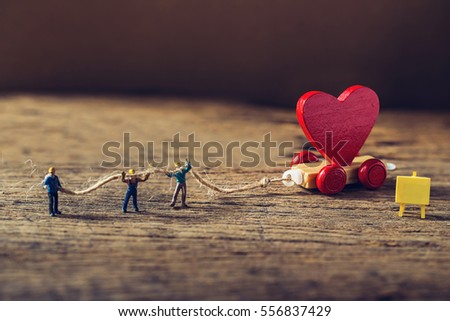 Miniature worker try to tow red heart shape of wooden toy train with sigh board on grunge wooden floor,Image for team building or love valentine day concept.