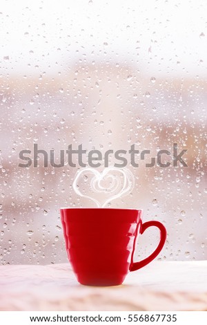 Steaming hot tea cup with heart shaped smoke on rainy background