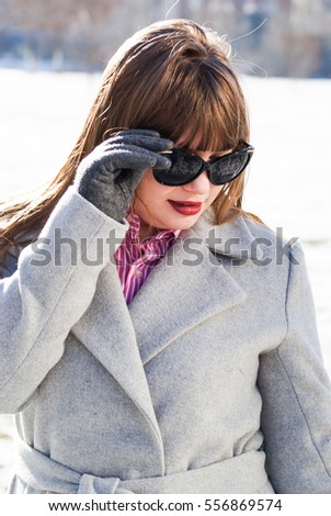 Beautiful long-haired girl in a fashionable gray coat wearing the black sunglasses during the cold season

