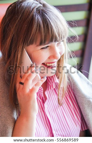 Beautiful long-haired girl in pink shirt talking on the phone in a cafe
