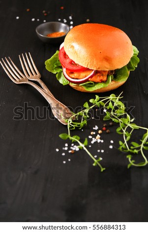 Delicious fresh homemade burger on dark serving board with spicy tomato sauce herbs over dark wooden background. Top view, copy space. 