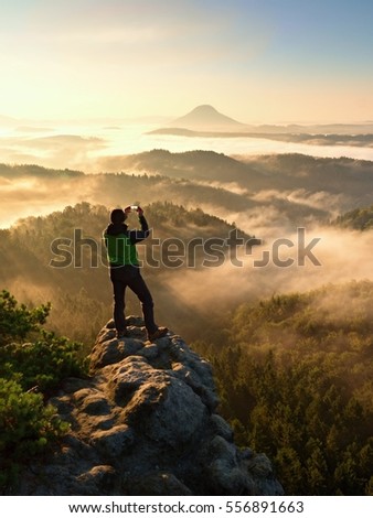 Tourist takes photos with smart phone on peak of hilly landscape. Autumn fogy hills, man photograph misty sunrise in hills and mountains.