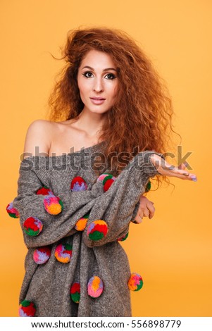 Attractive young woman with long red hair pointing away isolated over orange background