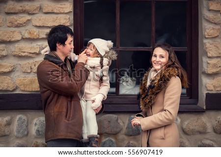 Happy family is standing near a window with a cat looking from the other its side in winter. Image with selective focus and toning