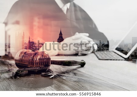 double exposure of justice and law concept.Male judge in a courtroom with the gavel,working with digital tablet computer docking keyboard on wood table,London architecture city
