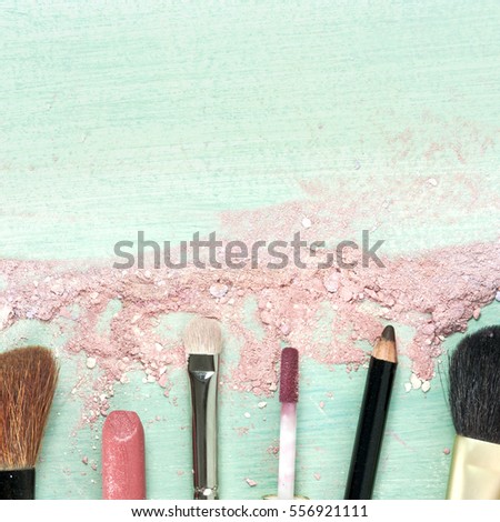 Makeup brushes and lipstick on a teal blue background, with traces of powder and blush on it. A square template for a makeup artist's business card or flyer design. With plenty of copyspace