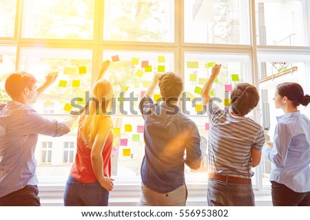 Students putting sticky notes on window for planning analysis Royalty-Free Stock Photo #556953802