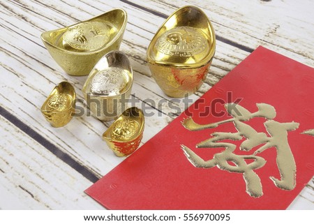 Gold ingots and red money packet for Chinese New Year festive on wooden Background. Chinese character means luck,wealth and prosperity as seen in the image.