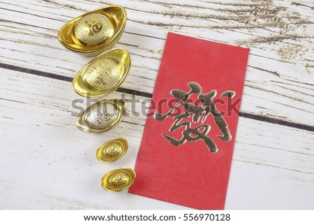 Gold ingots and red money packet for Chinese New Year festive on wooden Background. Chinese character means luck,wealth and prosperity as seen in the image.