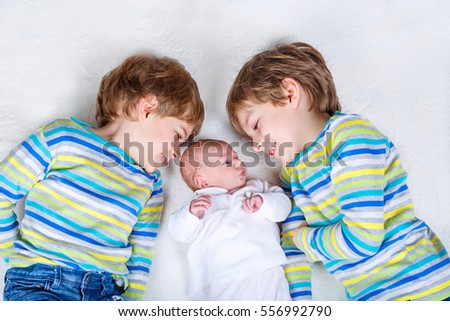 Two happy little preschool kids boys with newborn baby girl, cute sister. Siblings,, twins children and baby playing together. Kids bonding. Family of three, love.