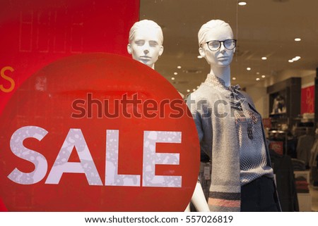 sale sign on shop window and fashion dolls in the store display clothes