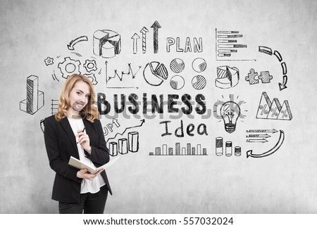 Cheerful redhead businesswoman with a notebook standing near a concrete wall with business idea icons