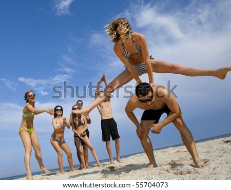 Young girl to jump across her boyfriend against joyful team of friends having fun at the beach