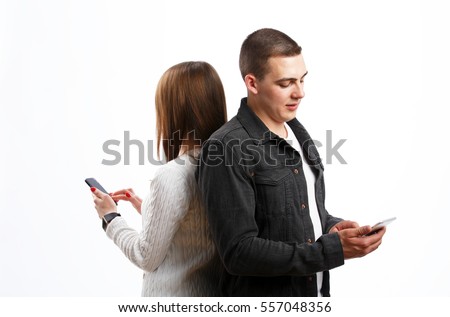 Beautiful young couple in casual clothing using smart phones and while standing back to back on white isolated background