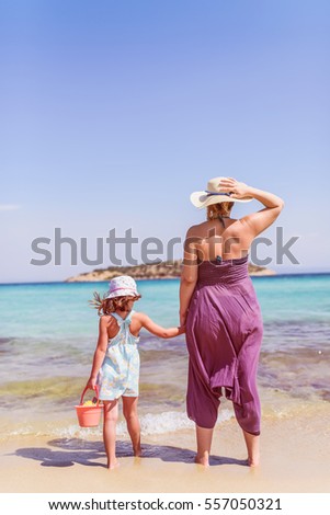 Back view of mother and daughter at tropical beach 