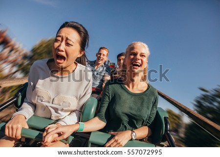 Shot of young friends cheering and riding roller coaster at amusement park. Young people having fun on rollercoaster. Royalty-Free Stock Photo #557072995