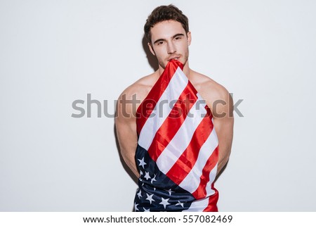Picture of young handsome man posing at studio and look at camera while holding USA flag. Isolated over white background.