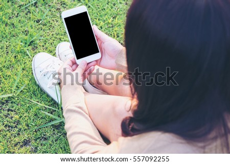Mockup image of a woman holding and using white mobile phone with blank black screen in green garden nature 