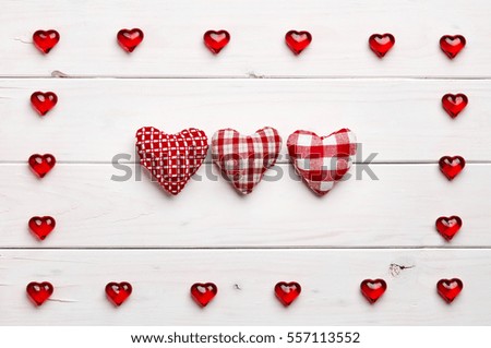 Texture of red heart shaped into frame with felt figures inside, on white wooden background 