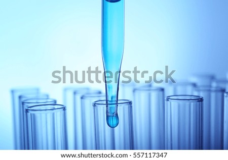 Closeup of a pipette dropping a sample into a test tube on light blue background