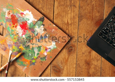 Palette and paintbrushes with notebook computer on wood background