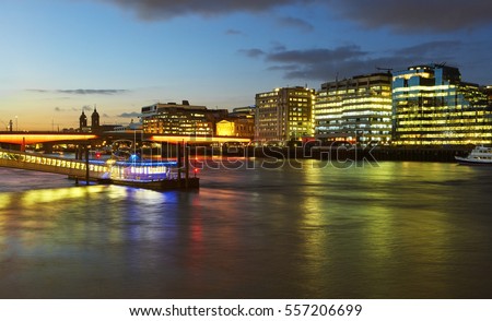 Skyline of the City of London illuminated at dusk with River Thames in foreground
