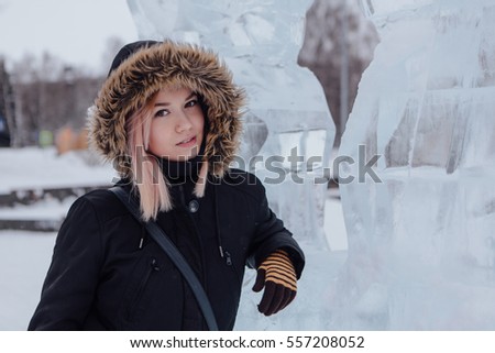 Winter fashion. Portrait of a beautiful young woman in warm clothes outdoor near the ice sculpture.