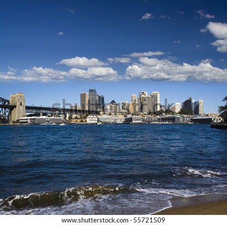 sydney australia quay side panoramic view over harbour blue water waves over sand coastline with cityscape of skyscrapers and blue sky