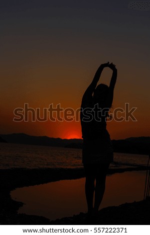 silhouette of a girl and a basket of flowers standing on the bank of a wide river in the rays of the setting of warm, beautiful sun