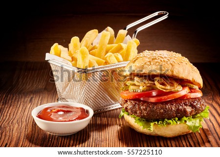 Studio shot of high burger with french fries in small fry basket and bowl of ketchup on wooden surface Royalty-Free Stock Photo #557225110